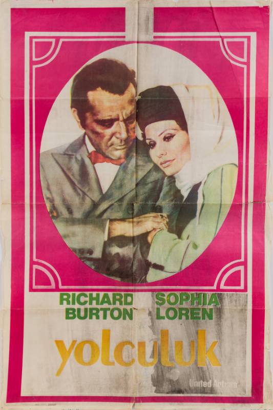 A poster of a man in a suit and bowtie and a woman in a black hat sitting closely holding hands.