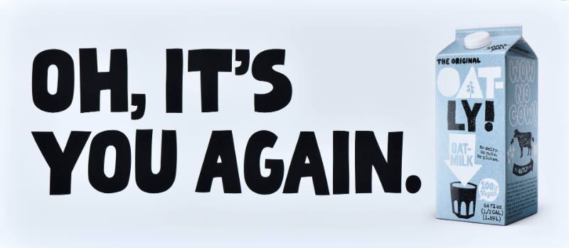 A poster with black text on a white background next to a carton of oatmilk