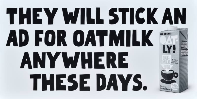 A poster with black text on a white background next to a carton of oatmilk