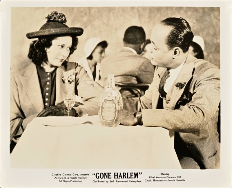 A printed card with a black and white photograph of a Black man and woman sitting a table looking at one another