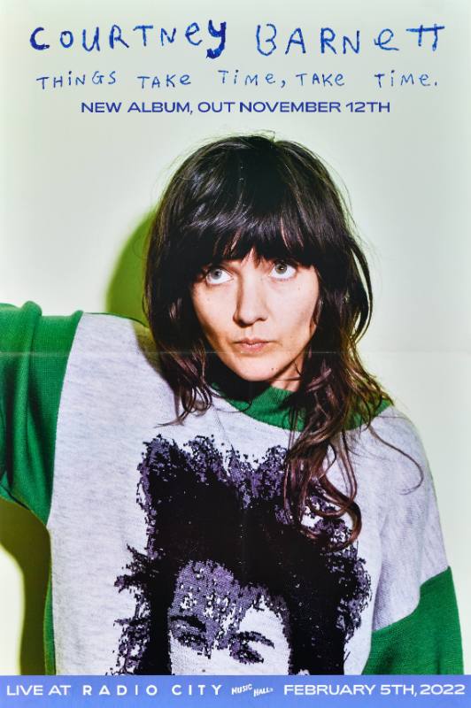 A poster of a dark haired woman wearing an oversized green and gray sweater looking upward.
